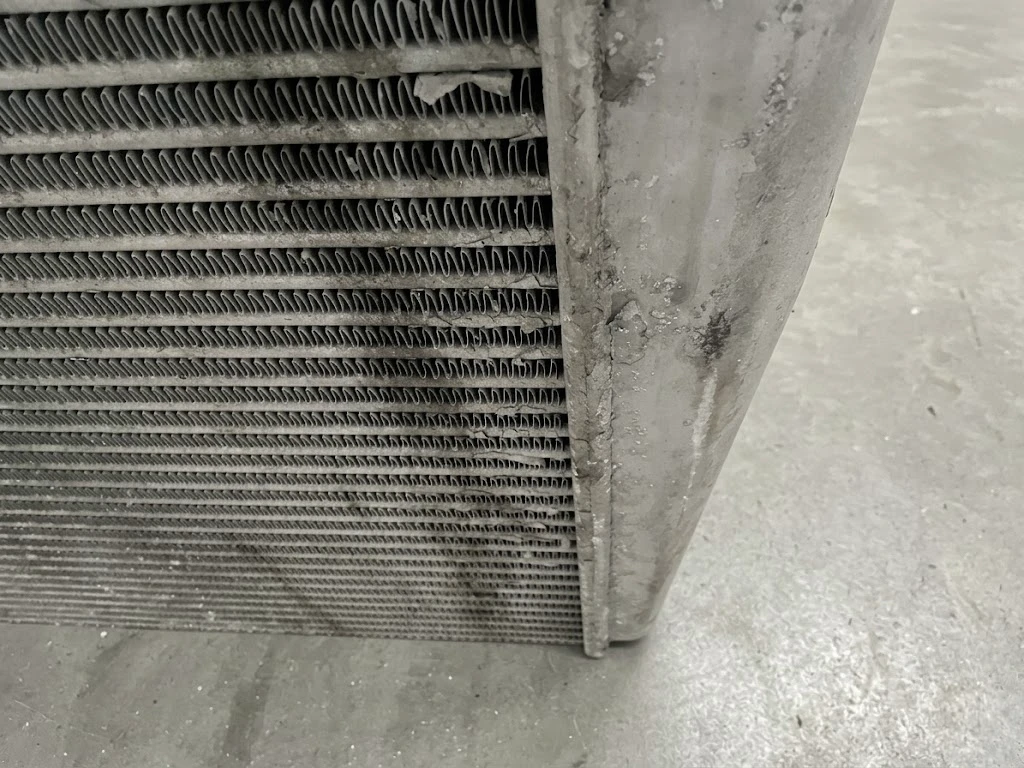Semi truck charge air cooler with heavily clogged fins covered in oil residue and road debris — reducing airflow and cooling efficiency