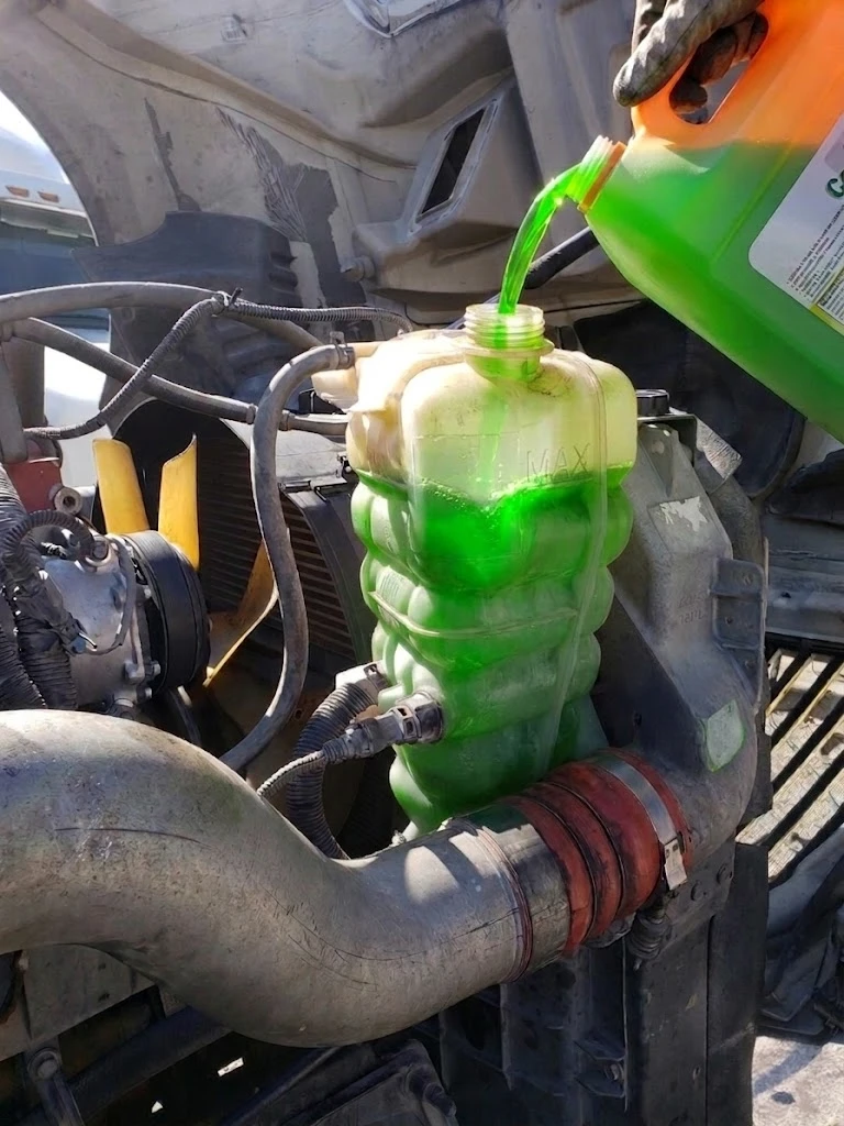 Fresh orange extended life coolant being poured into semi truck radiator fill neck — cooling system refill